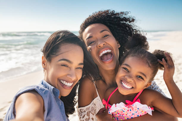 Two women and a little girl smiling on a beach.